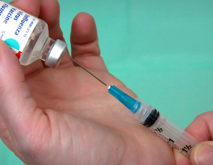 Inserting a syringe into a vial of influenza vaccine
