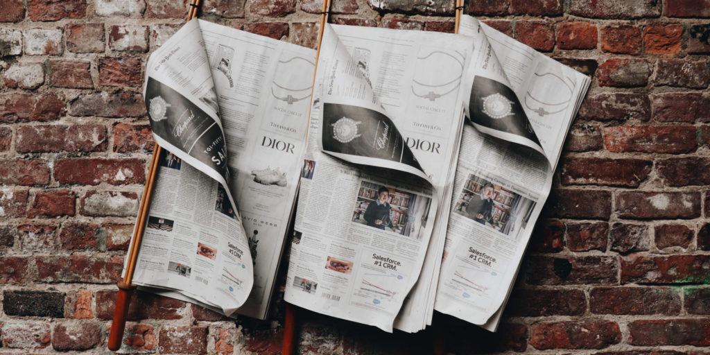 Three newspapers on reading sticks, hung on a brick wall